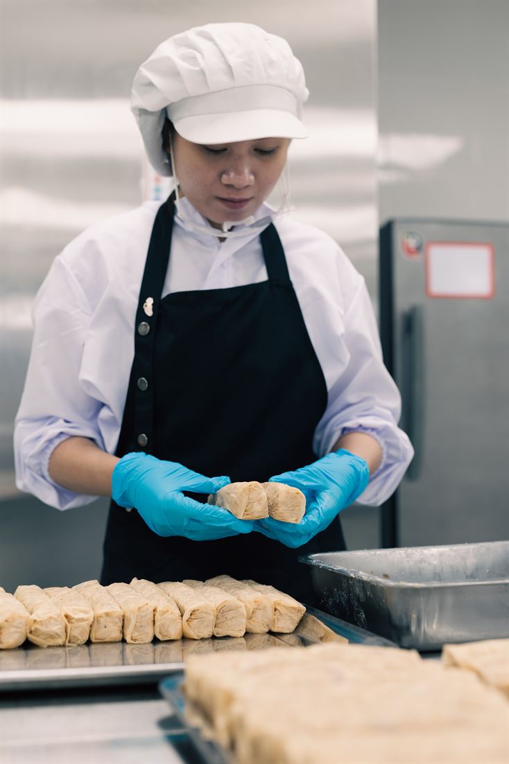A commissary worker hand-portioning prepared ingredients over a tray