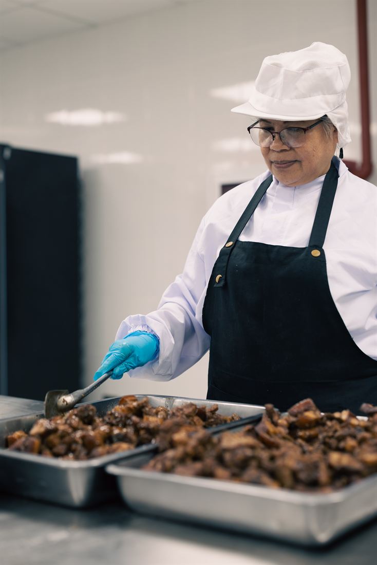 A smiling Kwatogs commissary cook plating trays of freshly braised meat