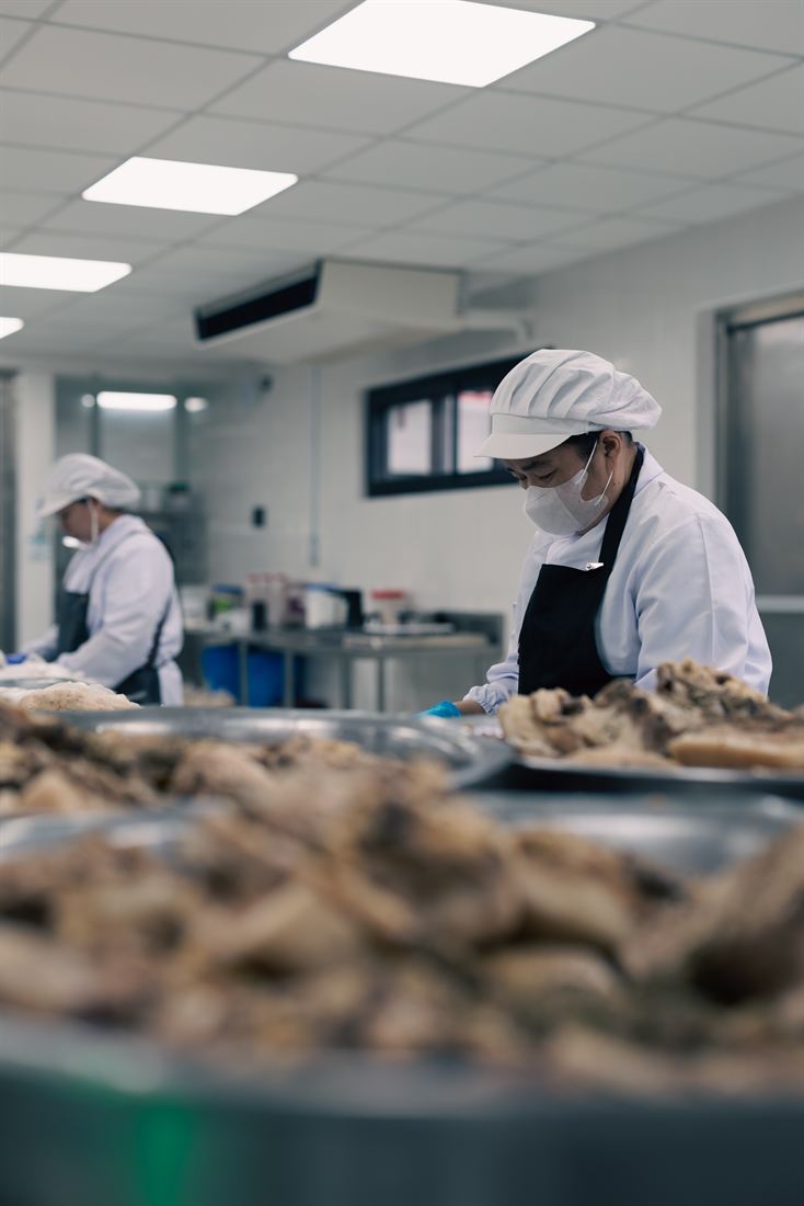 Kwatogs commissary staff in full food-safety gear working through trays of cooked meat